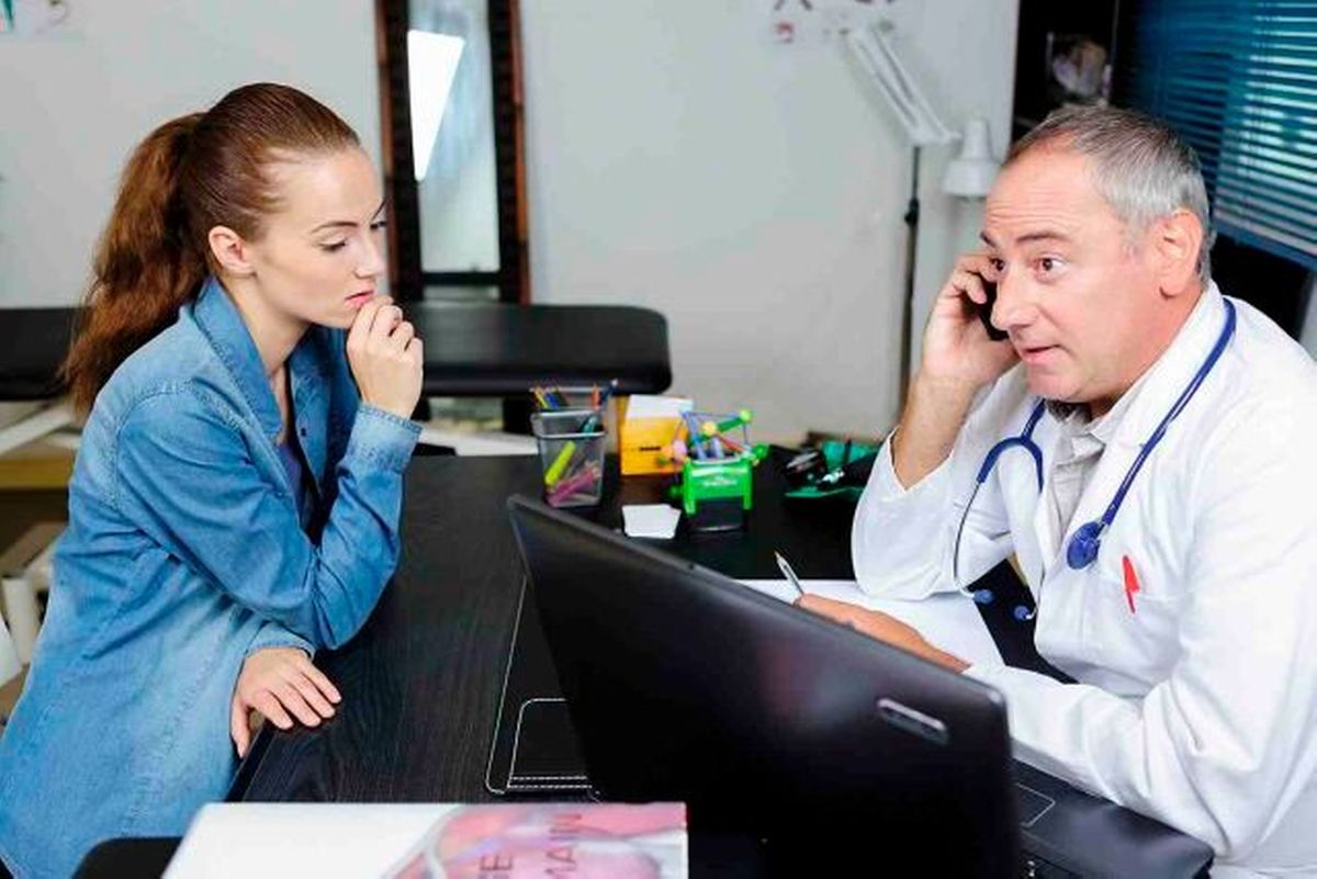 Junge Frau im Gespräch mit einem Arzt, der telefonisch Rücksprache hält